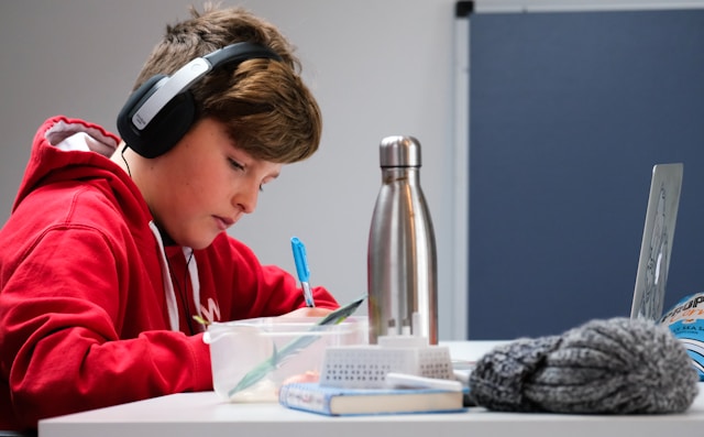 A young boy focused on doing his homework at a desk, surrounded by books and water bottle