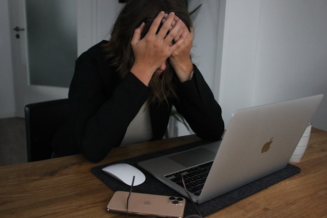 Woman sitting at a computer with her head in her hands, showing signs of stress and overwhelm.