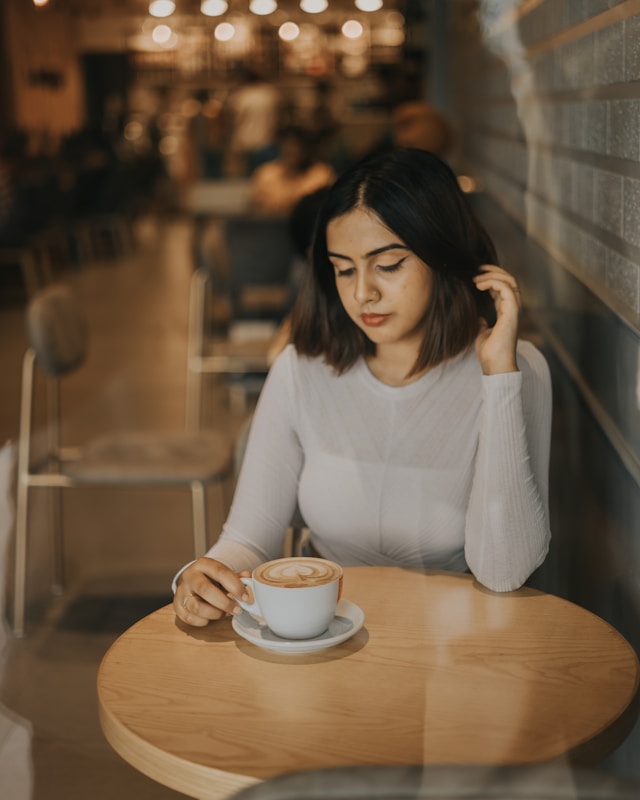 Woman sitting in a coffee shop holding a cup of coffee, representing reflection, calm, and the benefits of therapy for high achievers.