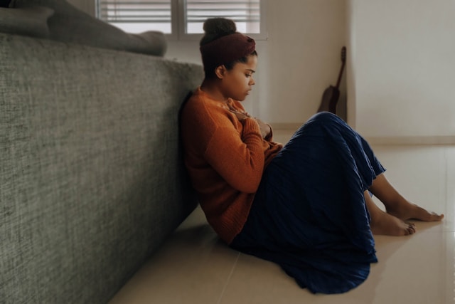 Woman sitting on the floor beside a couch looking distressed, representing the emotional and physical effects of anxiety