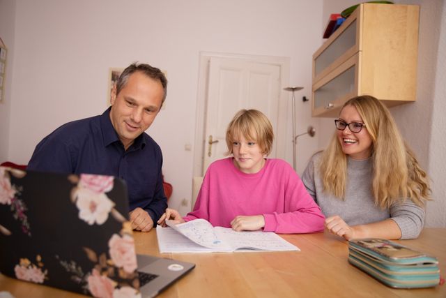 Child working on homework with parents while looking at a laptop