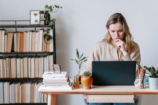 Thoughtful adult woman sitting at a desk with a laptop