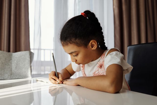 Young girl writing in a notebook while completing schoolwork at her desk