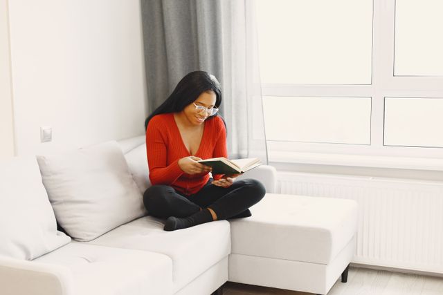 Woman sitting on a couch reading a book while enjoying a quiet moment at home