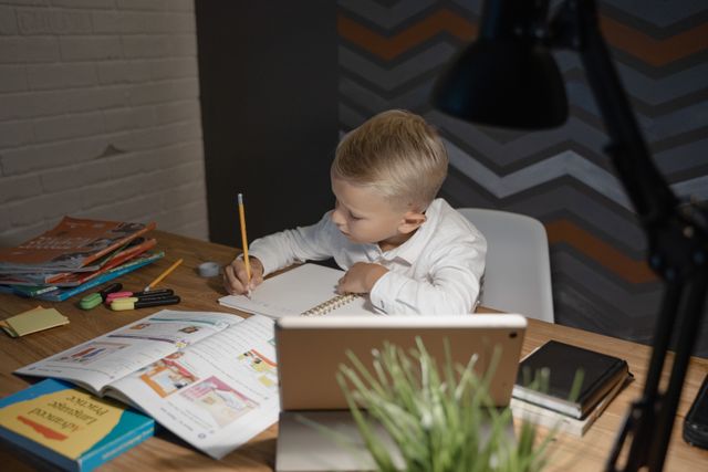 Young boy completing homework at a desk with school materials and a tablet