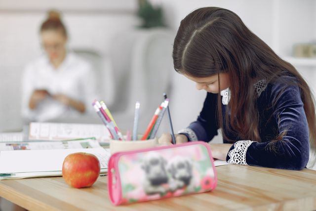 Young girl studying at a table with her mother nearby
